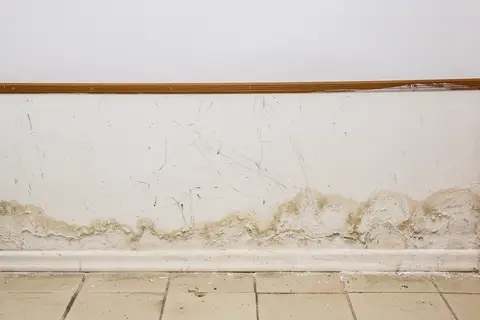 Feuchte Wand mit Feuchterand und Salzspuren im Sockelbereich über dem Fußboden