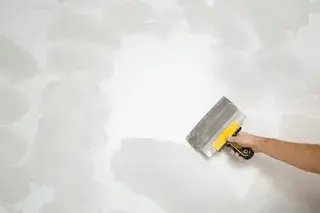 Hand trägt mit der Kelle Putz auf eine Wand auf